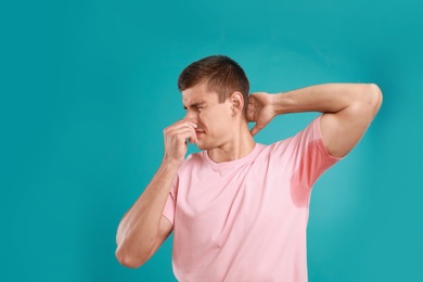 Photo of Young man with sweat stain on his clothes against light blue background. Using deodorant