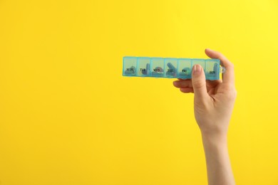 Photo of Woman holding plastic box with different pills on yellow background, closeup. Space for text