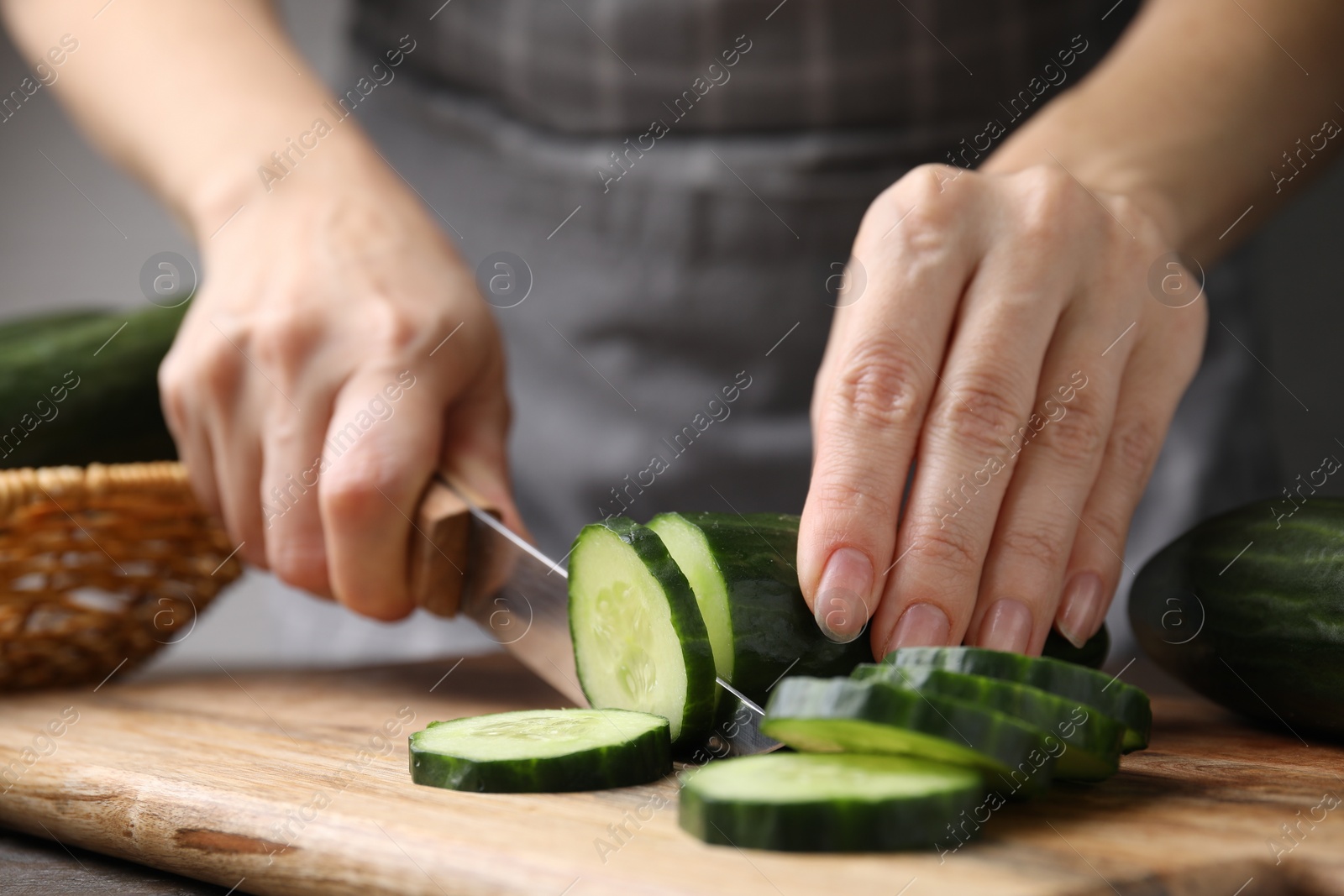 Photo of Woman cutting fresh cucumber at table, closeup