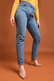 Woman in stylish jeans on brown background, closeup