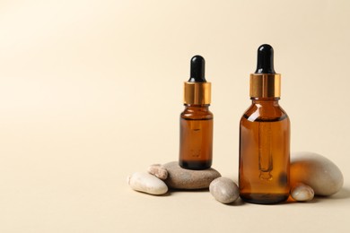 Photo of Bottles of cosmetic serum and stones on beige background. Space for text