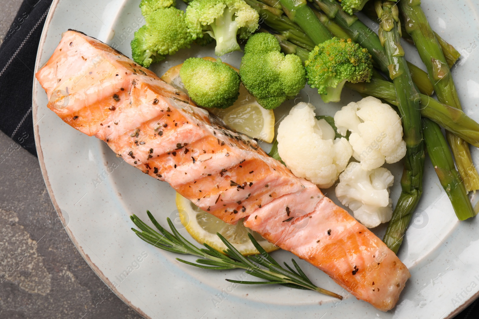 Photo of Healthy meal. Piece of grilled salmon, vegetables, asparagus and rosemary on grey textured table, top view