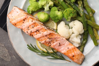 Photo of Healthy meal. Piecegrilled salmon, vegetables, asparagus and rosemary on grey textured table, top view