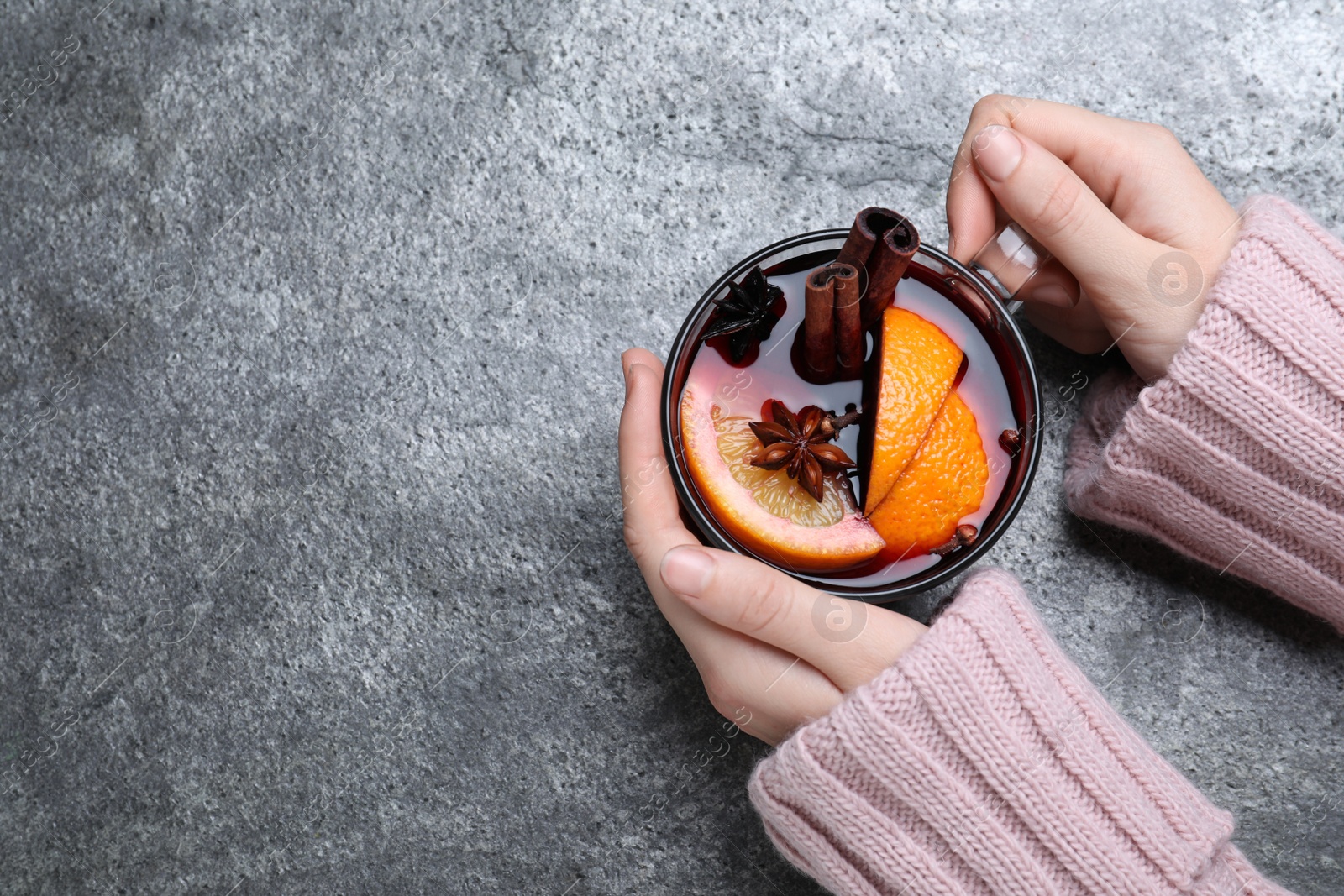 Photo of Woman with glass cup of mulled wine at grey table, top view. Space for text