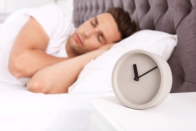 Young man sleeping in bed and alarm clock on nightstand at home