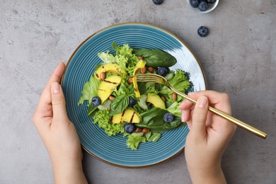 Photo of Woman eating avocado salad with blueberries at light grey table, top view