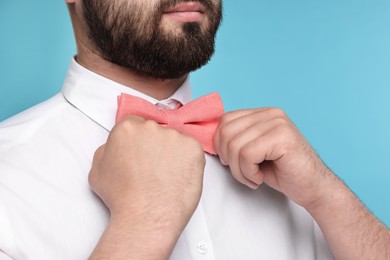 Photo of Man in shirt adjusting bow tie on light blue background, closeup