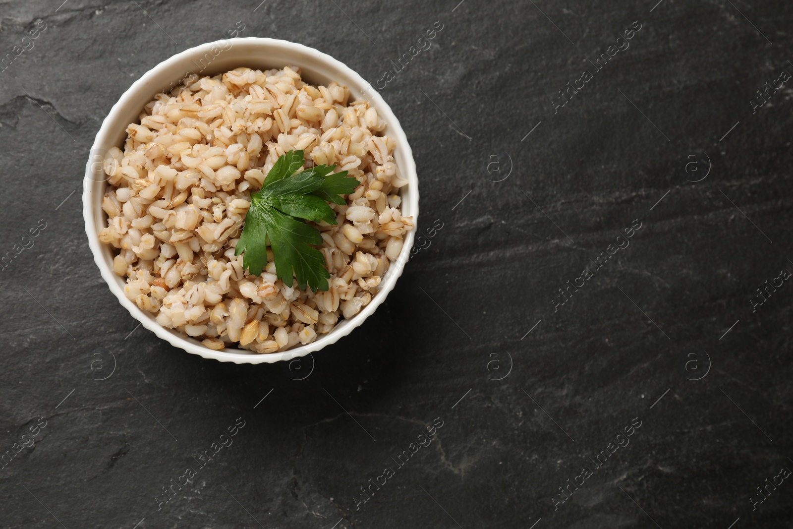 Photo of Tasty pearl barley porridge in bowl on dark textured table, top view. Space for text