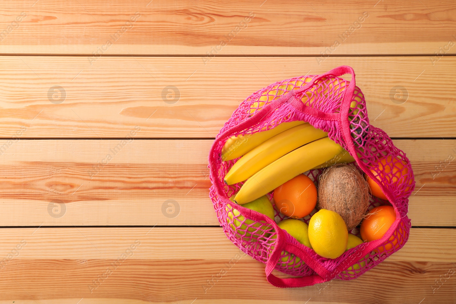 Photo of Net bag with fruits on wooden table, top view. Space for text