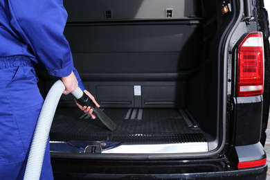 Photo of Worker using vacuum cleaner in automobile trunk at car wash, closeup