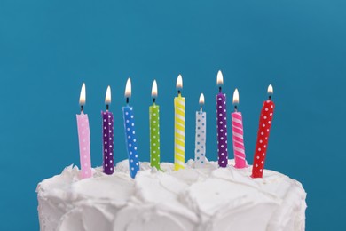 Delicious cake with cream and burning candles on light blue background, closeup