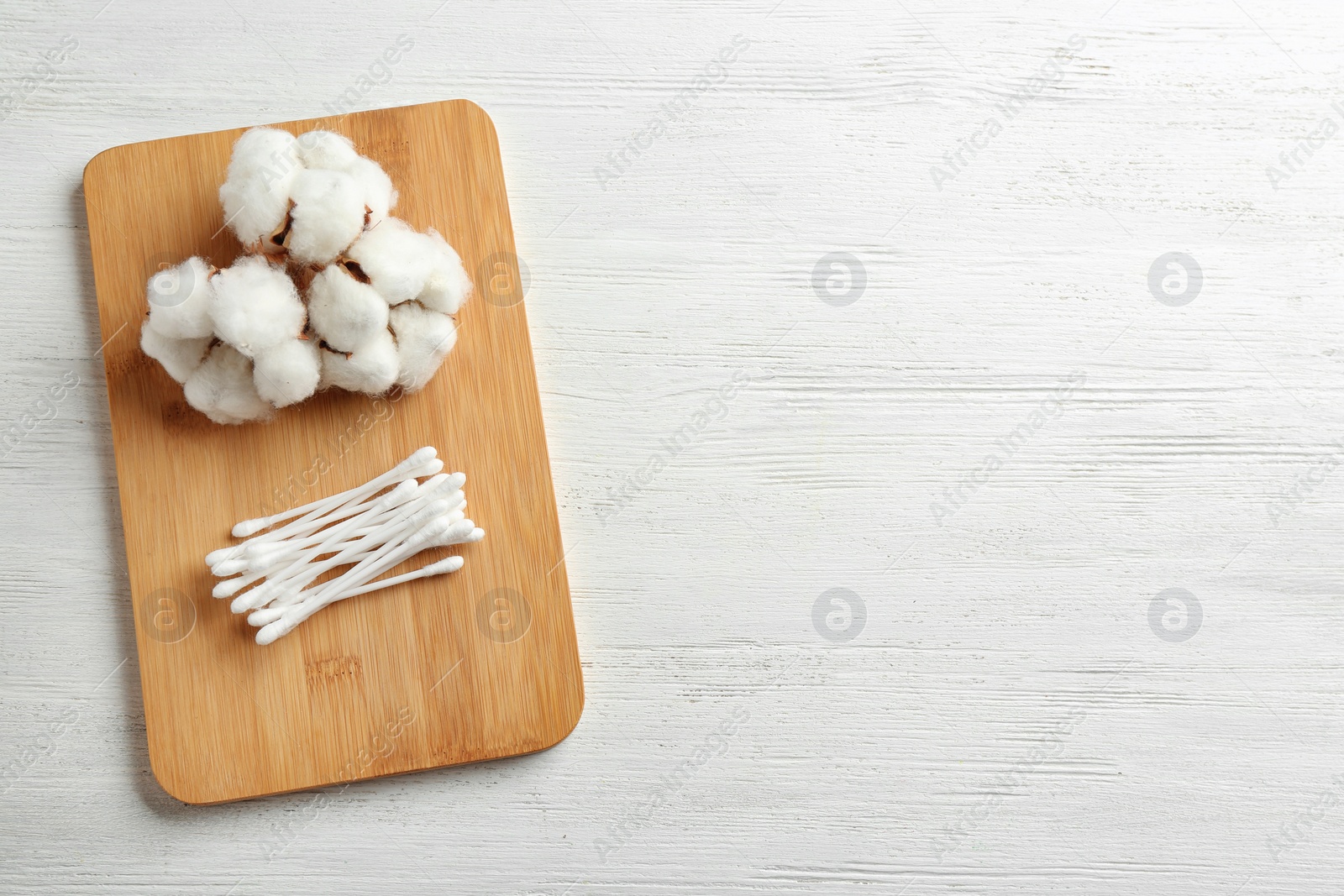 Photo of Board with cotton swabs and flowers on white wooden background, top view. Space for text