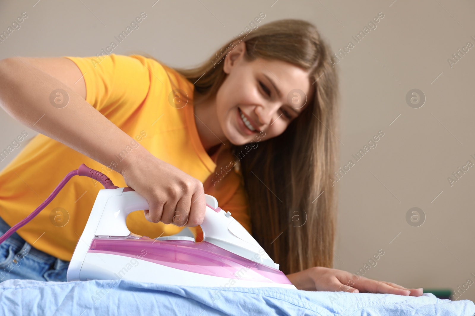 Photo of Young woman ironing shirt on board at home