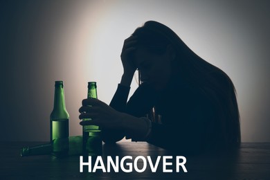 Image of Suffering from hangover. Woman holding bottle of beer at table
