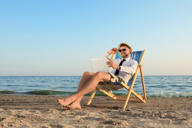 Photo of Happy man with laptop resting on deckchair near sea. Business trip