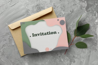 Photo of Beautiful card with word Invitation, envelope and eucalyptus leaves on grey table, flat lay