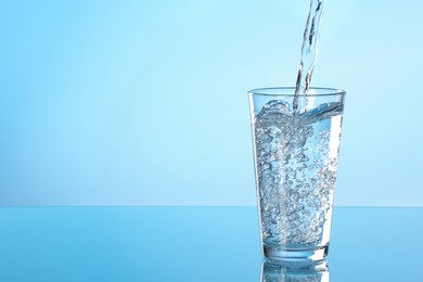 Photo of Pouring water into glass on light blue background. Space for text