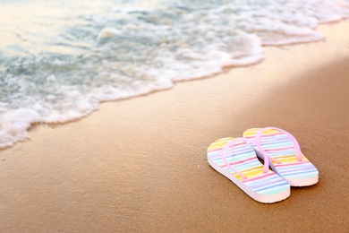 Photo of Stylish flip flops on sand near sea, space for text. Beach accessories