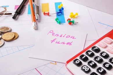 Photo of Paper note with text PENSION FUND, calculator and stationery on table