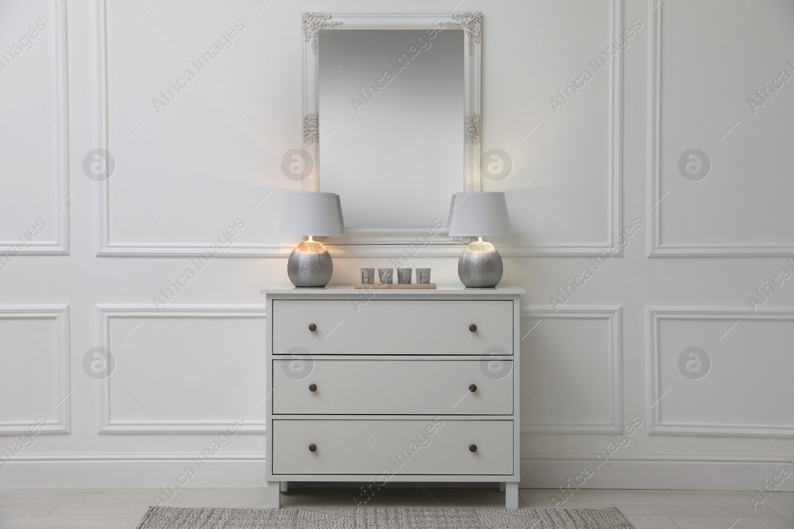 Photo of White chest of drawers with lamps near mirror in room. Interior design