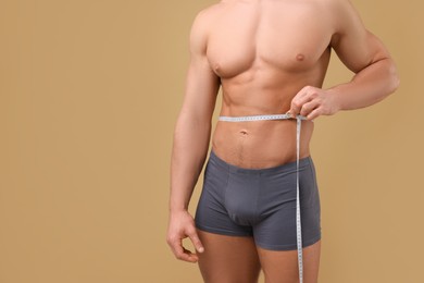 Photo of Athletic man measuring waist with tape on brown background, closeup and space for text. Weight loss concept