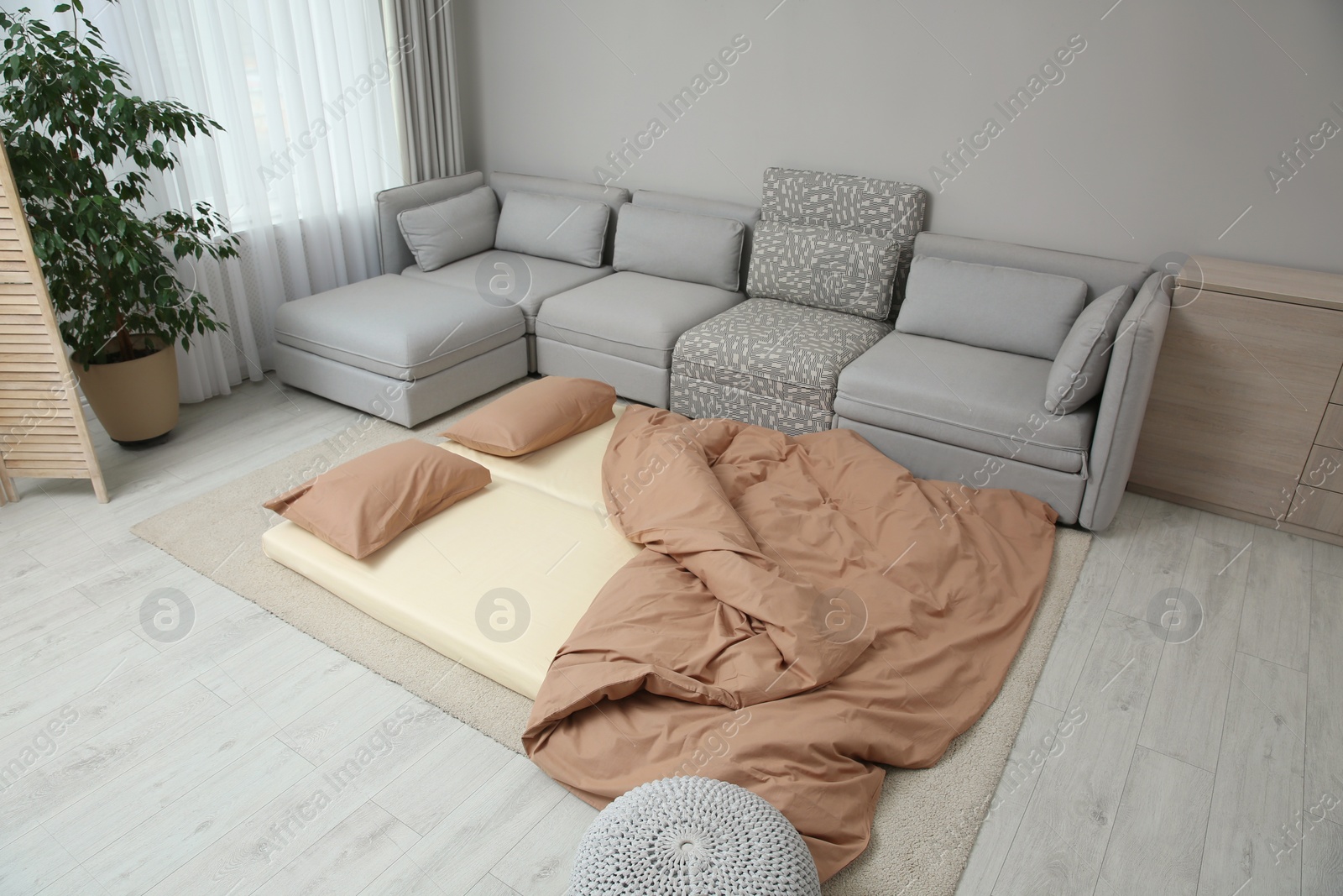 Photo of Mattress with pillows and blanket on floor near sofa. Additional sleep place for guest