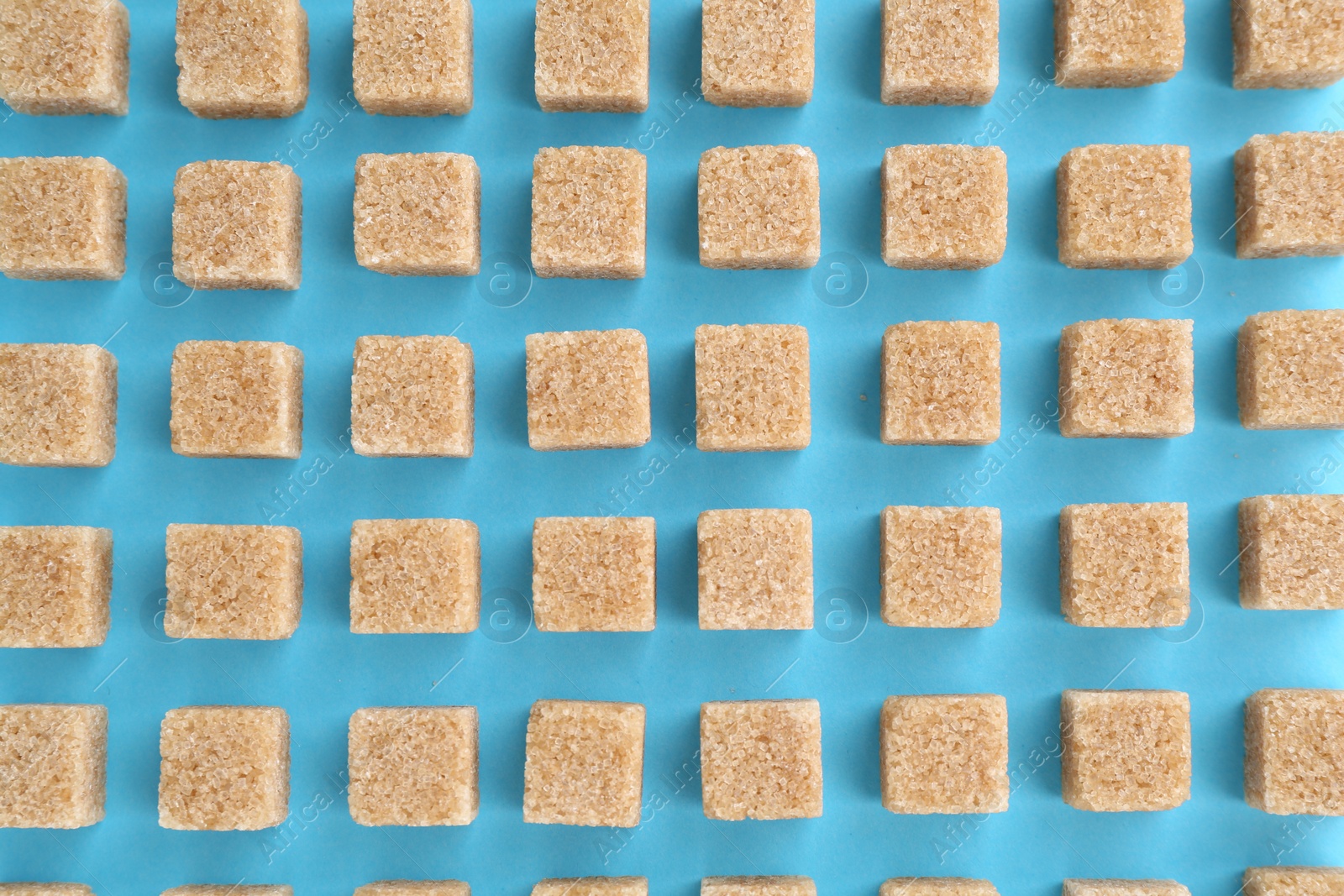 Photo of Brown sugar cubes on light blue background, top view