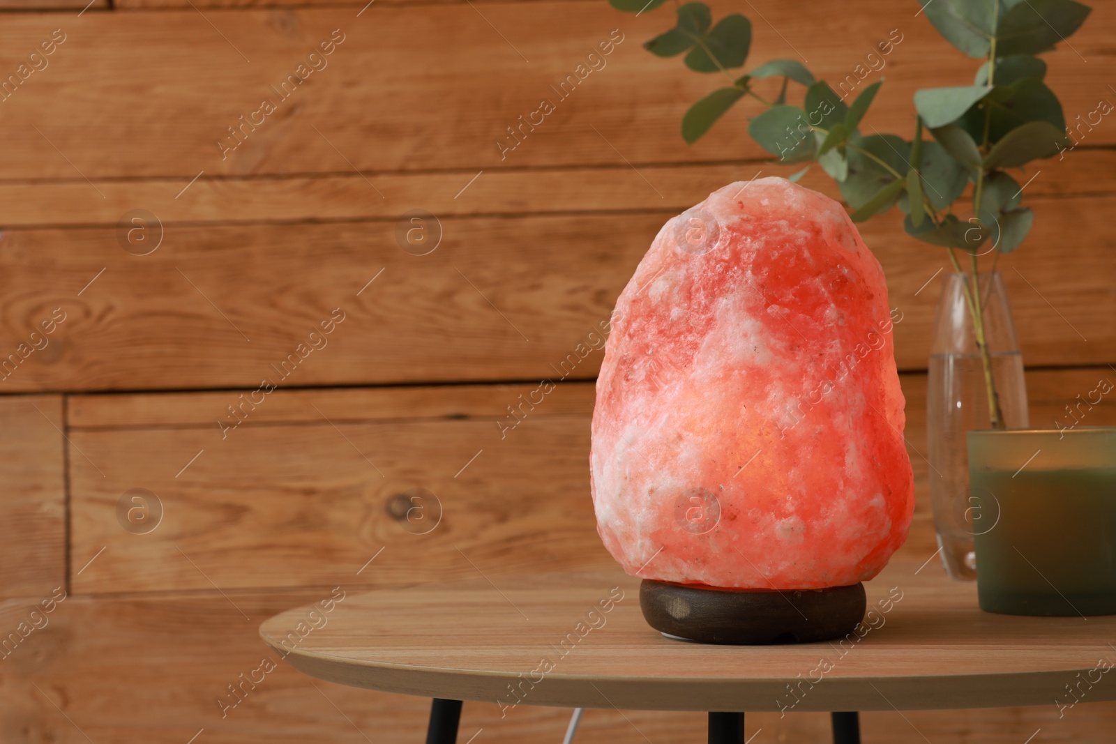 Photo of Beautiful Himalayan salt lamp, eucalyptus branches and candle on wooden table indoors, space for text