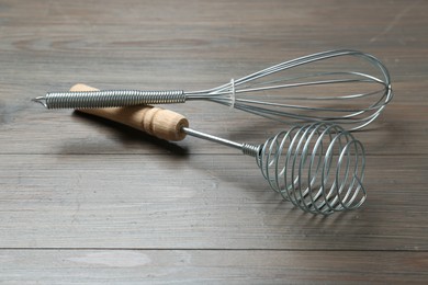 Two metal whisks on wooden table, closeup