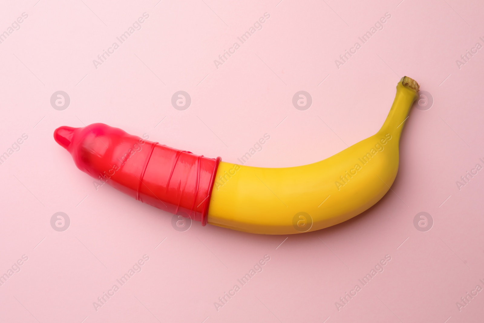 Photo of Banana with condom on pink background, top view. Safe sex concept