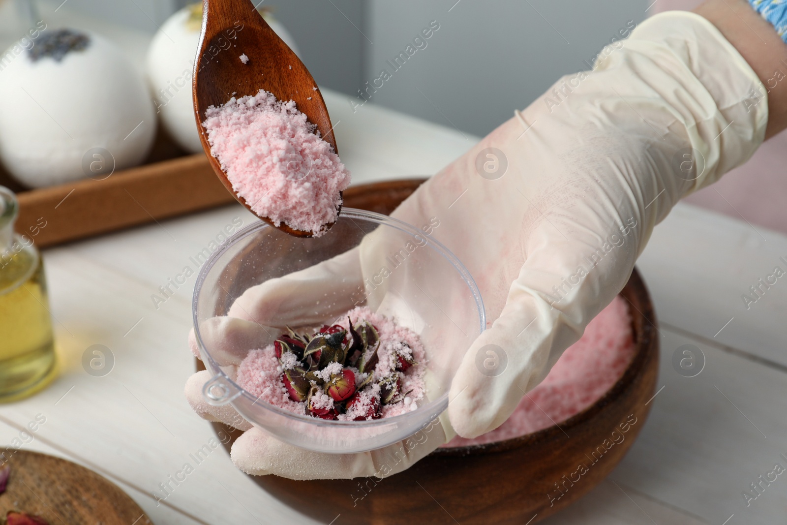 Photo of Woman in gloves making bath bomb at white table, closeup