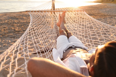 Photo of Man relaxing in hammock on beach at sunset
