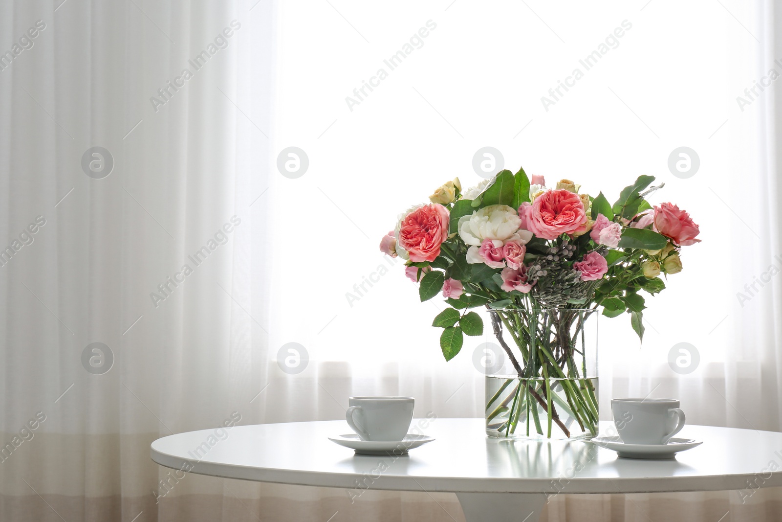 Photo of Vase with beautiful flower bouquet and cups of coffee on table in room. Space for text