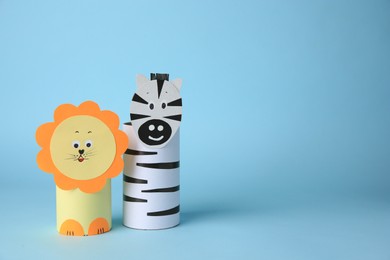Toy lion and zebra made from toilet paper hubs on light blue background, space for text. Children's handmade ideas