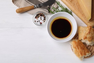 Bowl of balsamic vinegar with oil, bread and spices on white wooden table, flat lay. Space for text