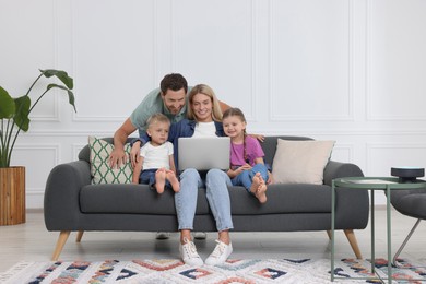Photo of Happy family with laptop spending time together on sofa at home