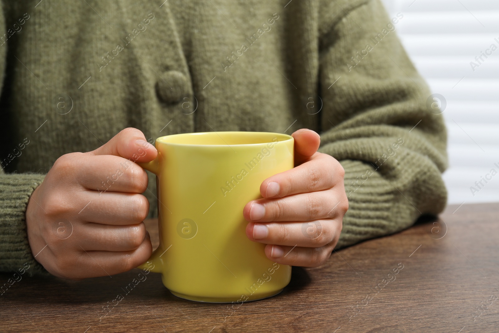 Photo of Woman holding yellow mug at wooden table, closeup