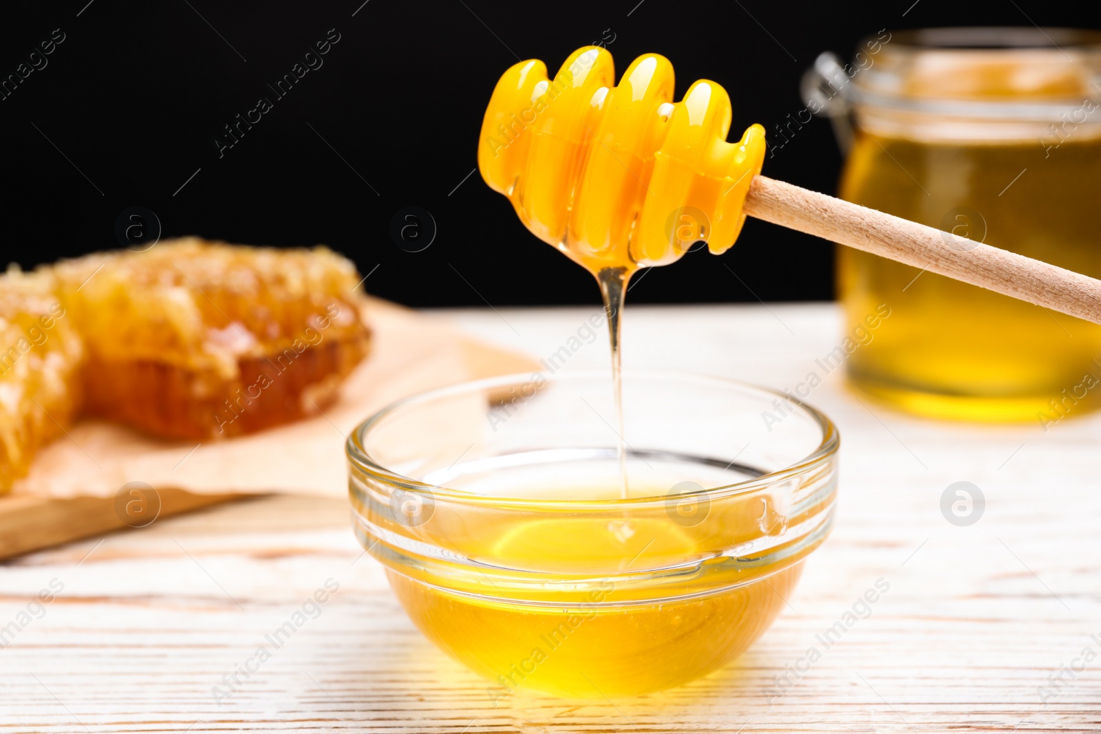 Photo of Honey dripping from dipper into bowl on white wooden table