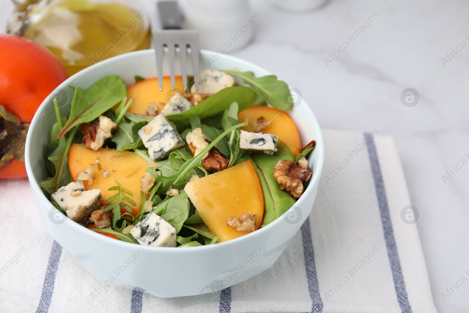 Photo of Tasty salad with persimmon, blue cheese and walnuts served on white marble table, closeup. Space for text