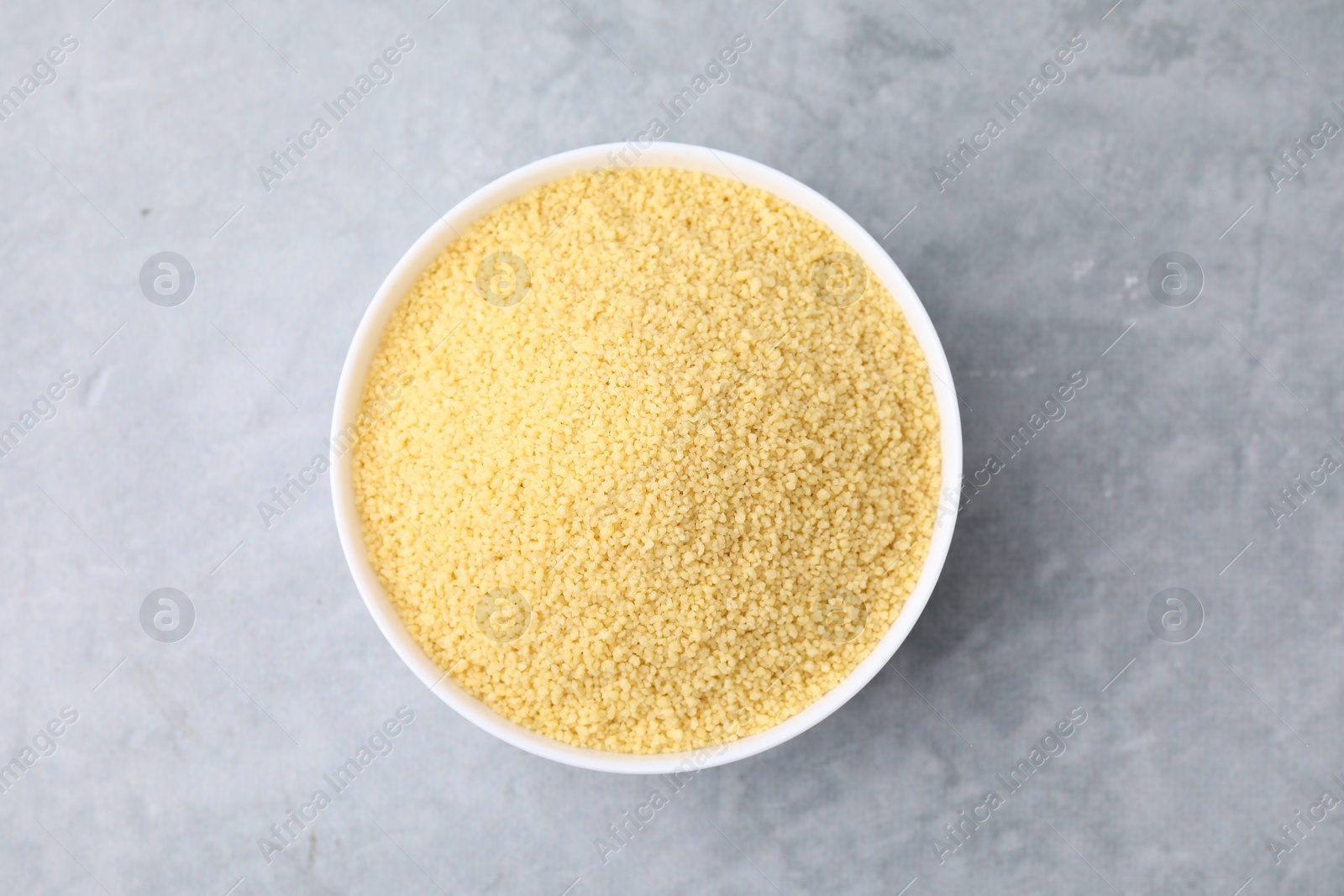 Photo of Raw couscous in bowl on gray table, top view