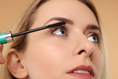 Beautiful woman applying mascara on beige background, closeup