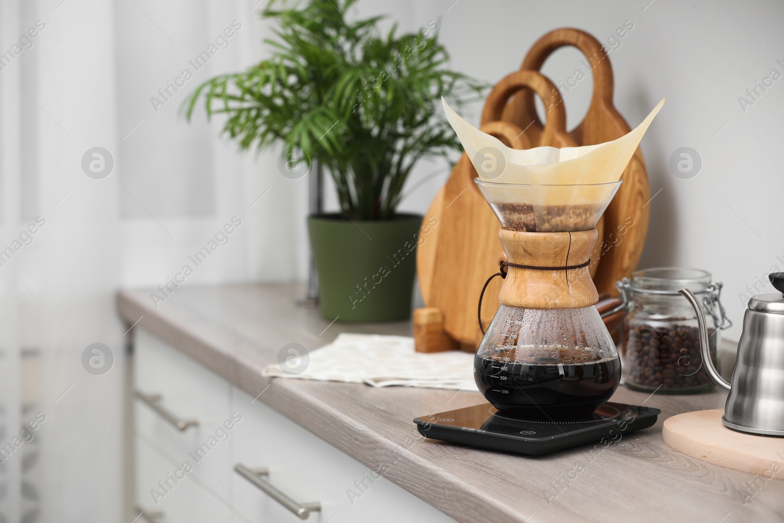 Photo of Glass chemex coffeemaker with paper filter and coffee on wooden countertop in kitchen, space for text