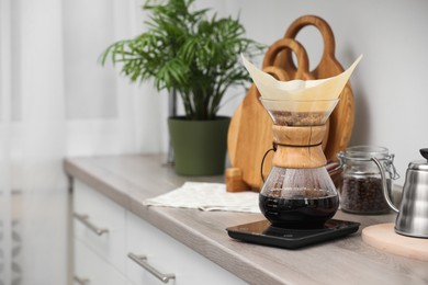 Photo of Glass chemex coffeemaker with paper filter and coffee on wooden countertop in kitchen, space for text