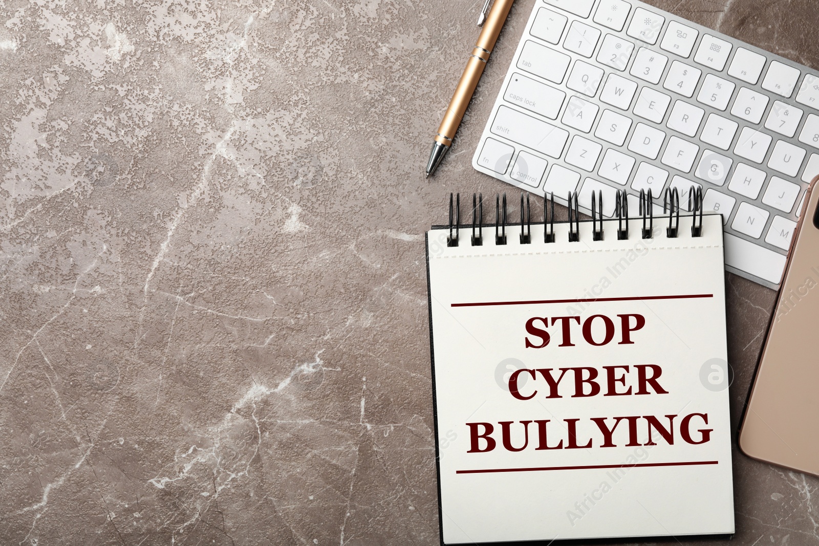 Image of Notebook with phrase STOP CYBER BULLYING and keyboard on grey marble table, flat lay. Space for text