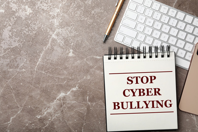 Notebook with phrase STOP CYBER BULLYING and keyboard on grey marble table, flat lay. Space for text