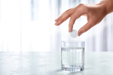 Woman putting tablet into glass of water indoors, space for text