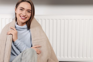 Woman with blanket near heating radiator indoors, space for text