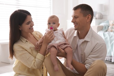 Photo of Happy couple holding their cute little baby with pacifier at home