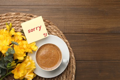 Image of Apology. Note with word Sorry, beautiful yellow freesias and cup of coffee on wooden table, flat lay. Space for text