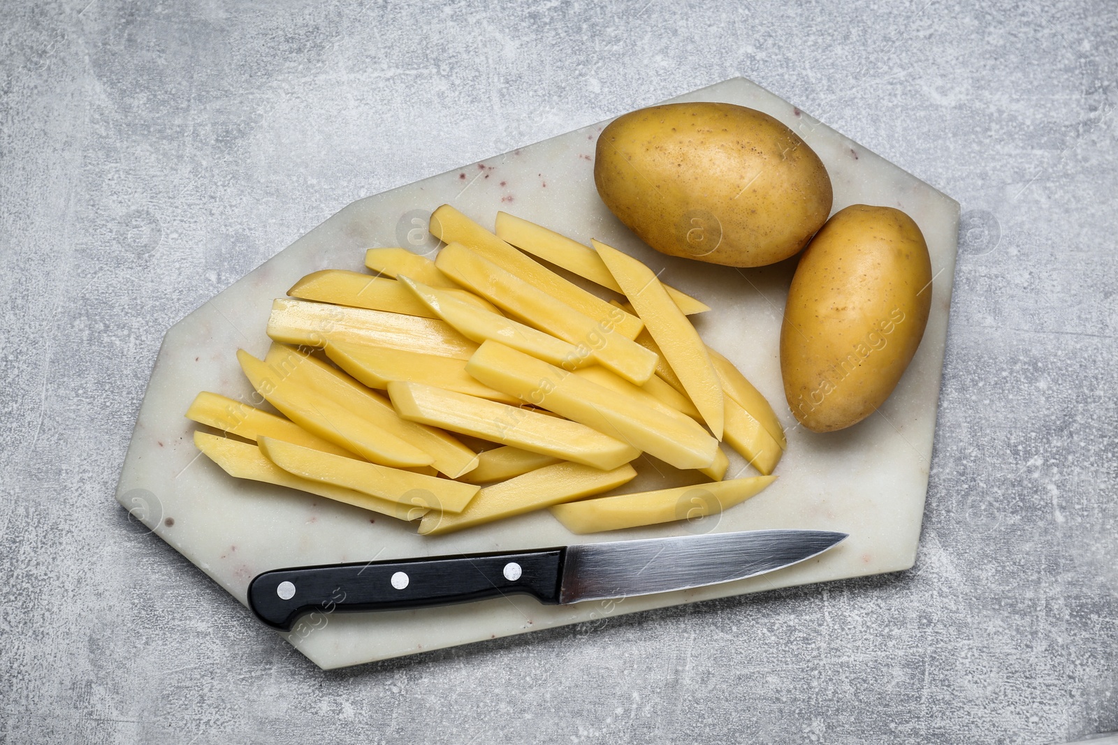 Photo of Whole and cut raw potatoes with knife on light grey table, top view. Cooking delicious French fries